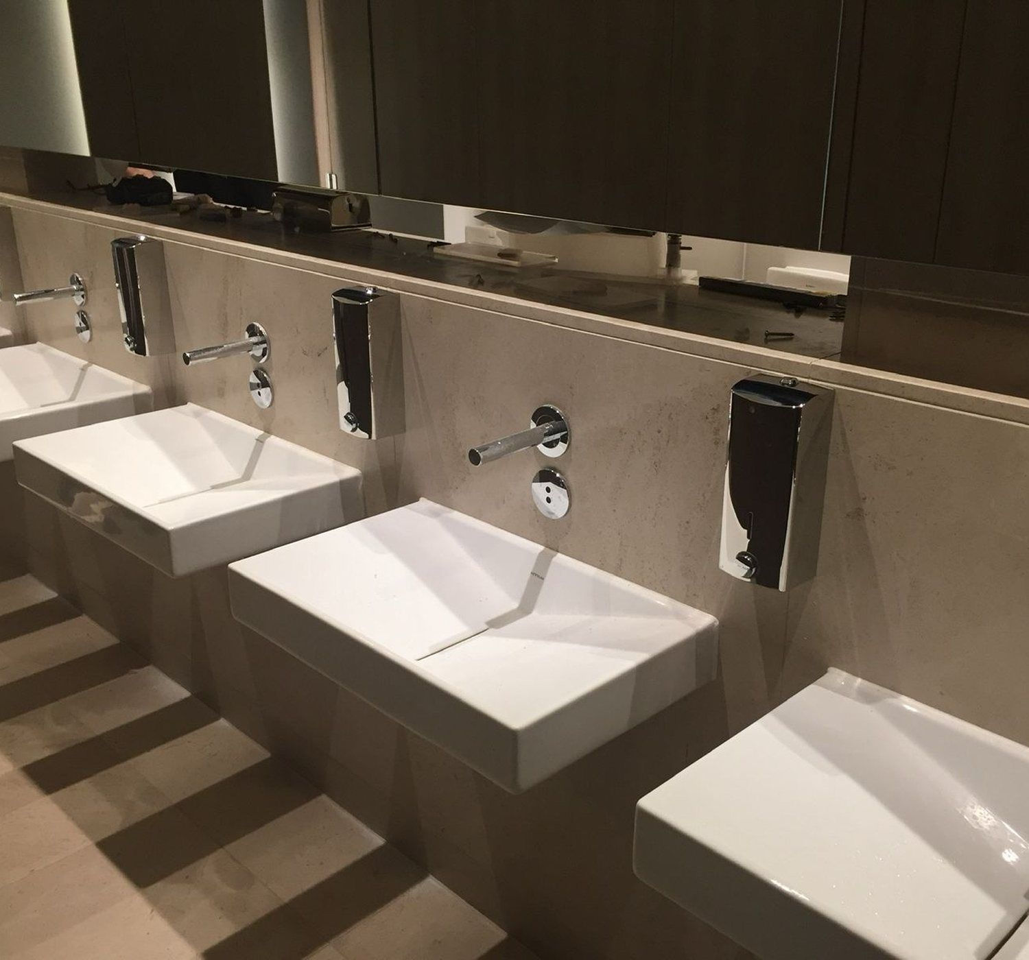 Hotel public washroom during installation, wall-hung basins fitted and tools still on the counter