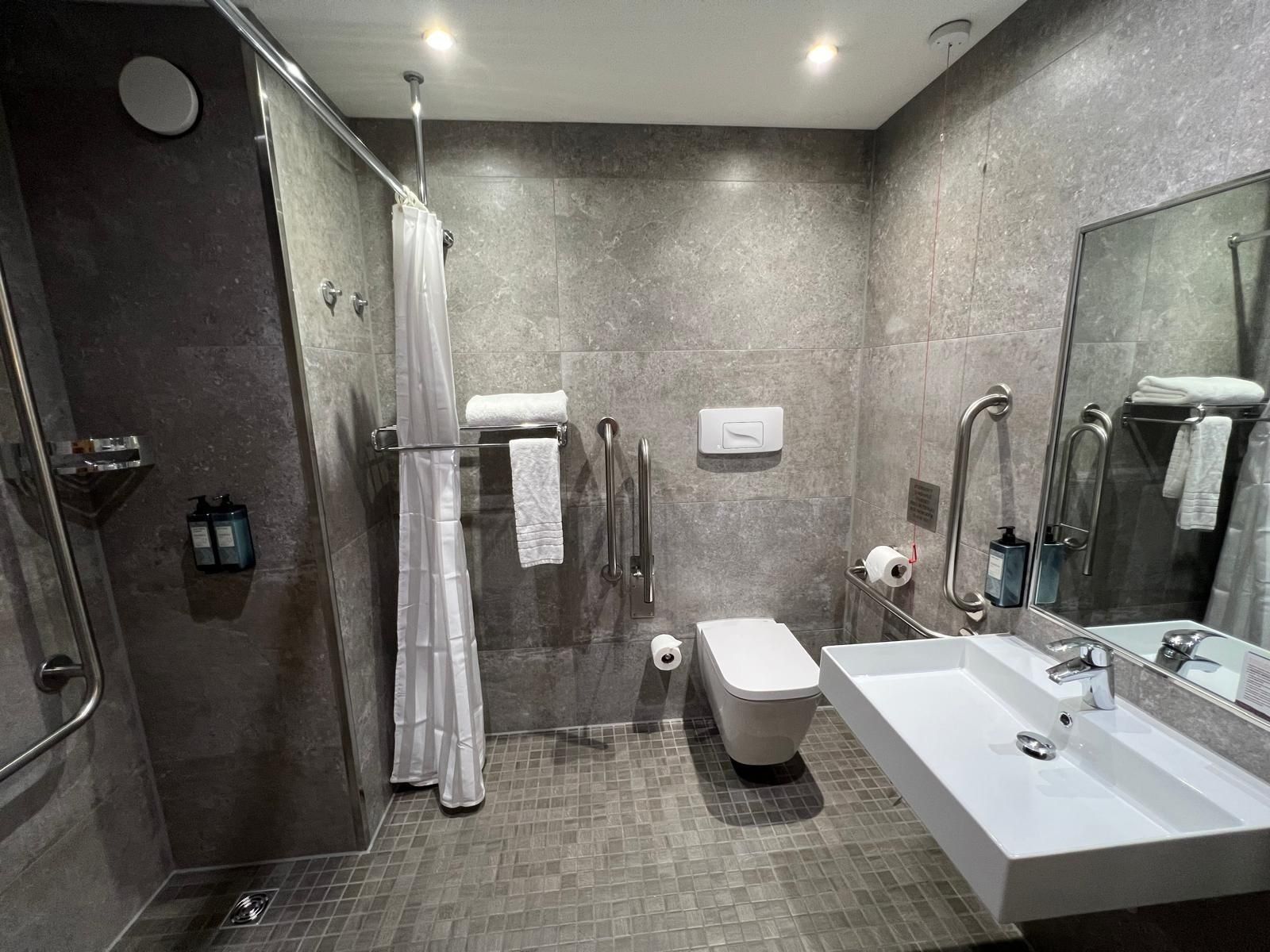 Accessible hotel bathroom with level-access shower, grab rails and emergency pull cord
