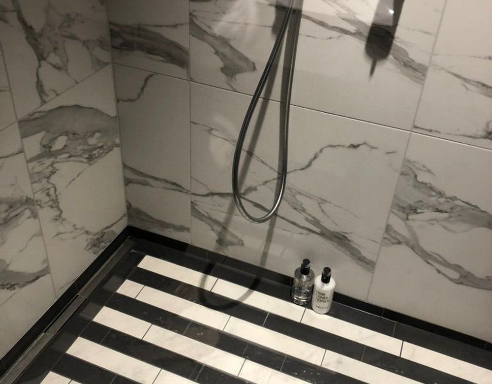 Shower floor detail with striped black and white marble mosaic and a linear drain