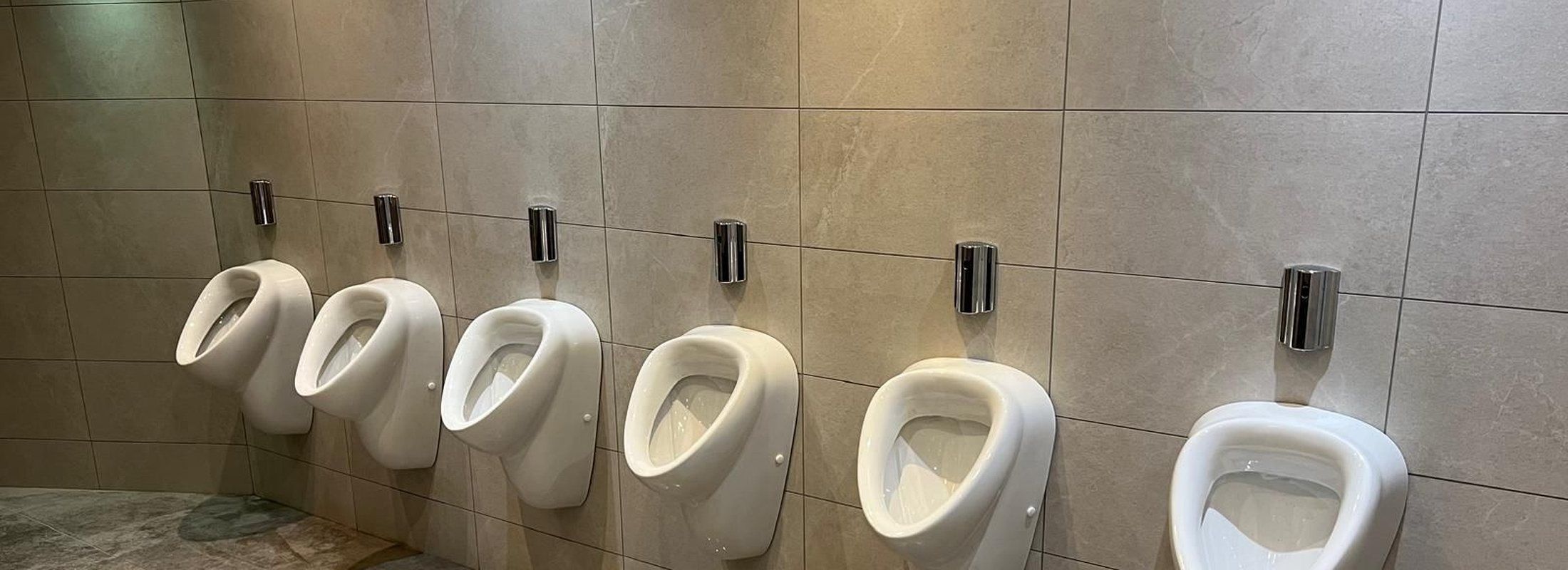 Refurbished public washroom in a hotel with tiled walls and a row of urinals